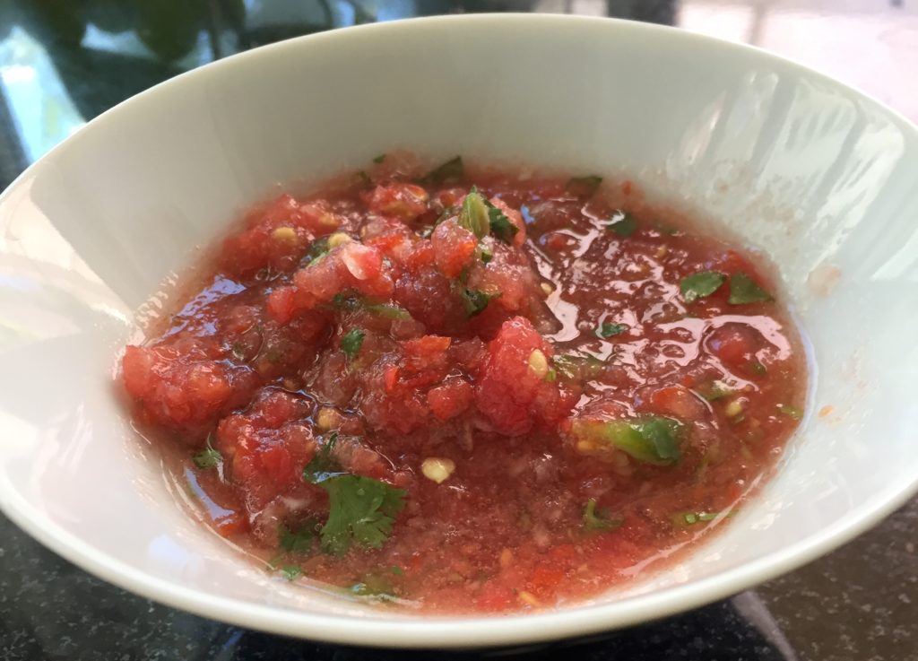 a bowl of homemade tomato salsa, with tomatoes, onions, jalapeño, and cilantro.