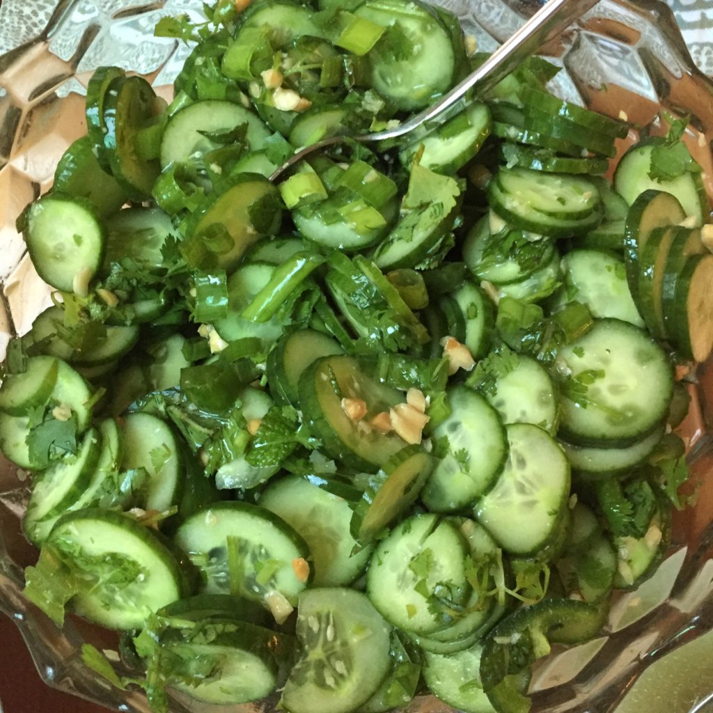 Glass bowl with cucumber salad, including peanuts, cilantro, and jalapeños.